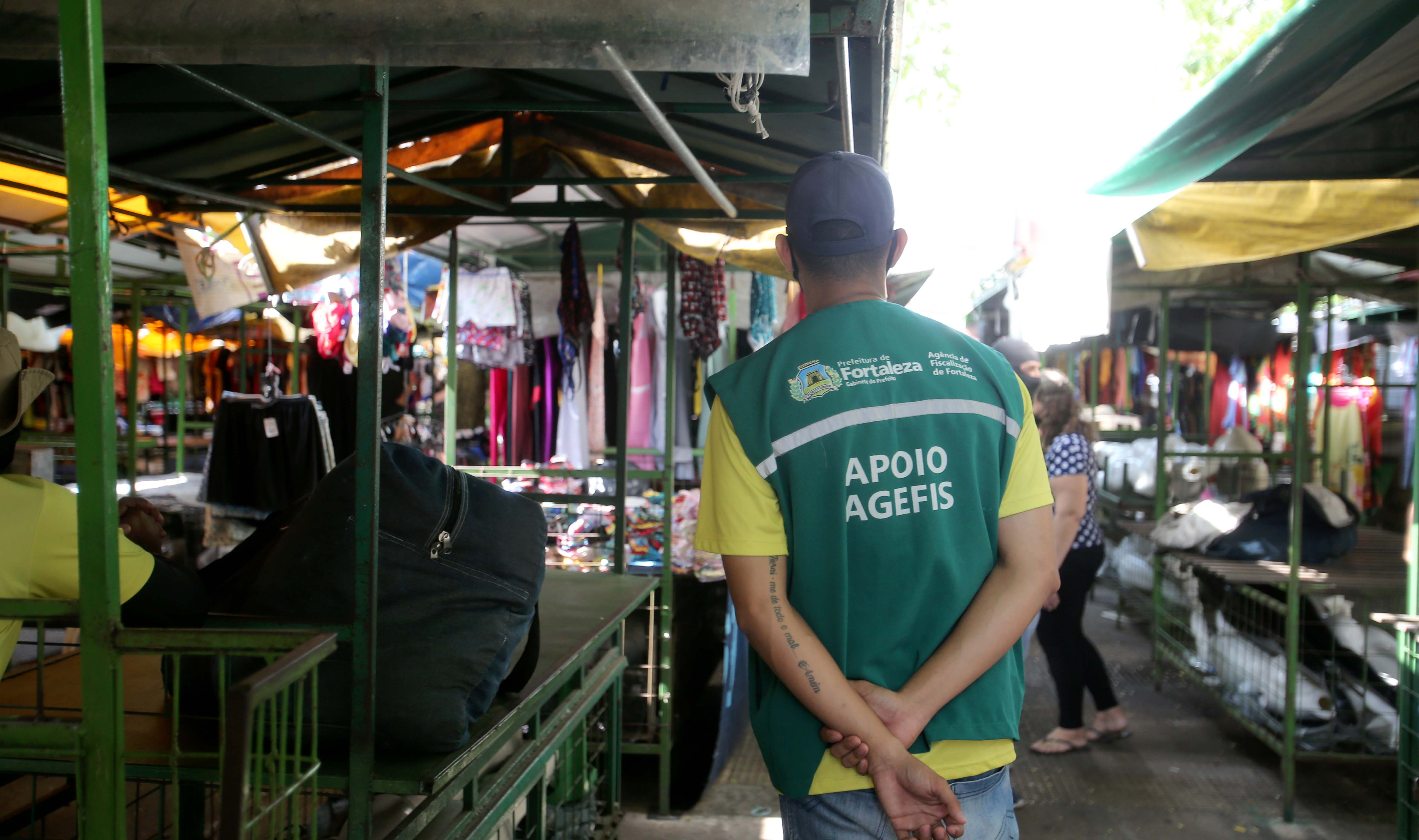 agente da agefis de costas em frente a uma barraca de feira